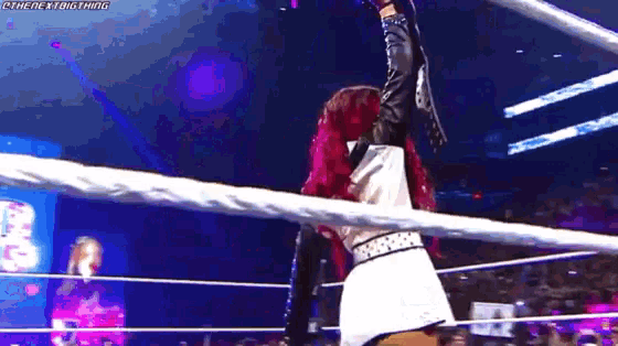 a woman is hanging from a rope in a wrestling ring while a referee looks on .