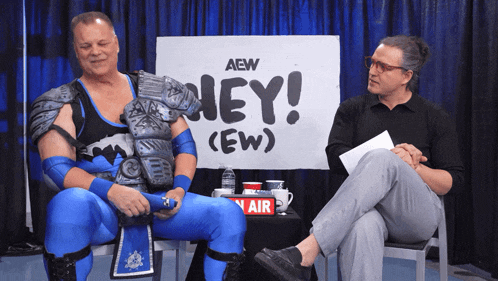 two men are sitting in front of a sign that says hey ( ew )