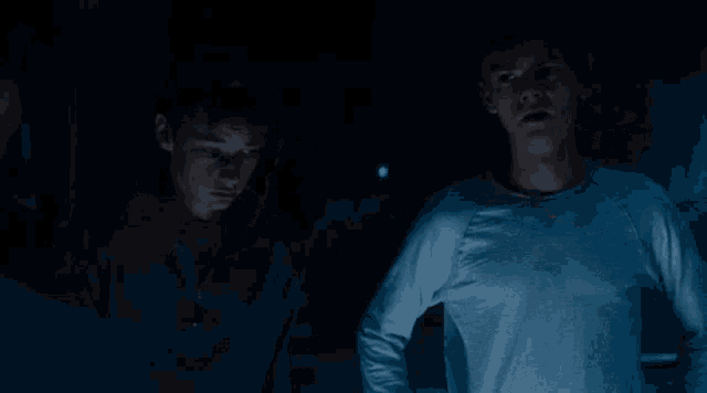 two young men are standing in a dark room looking at something