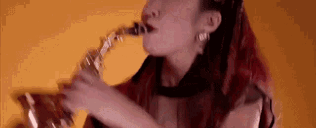 a woman with red hair is playing a saxophone against a yellow wall .