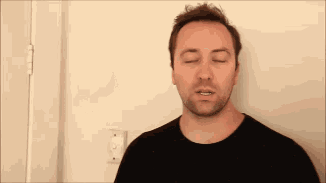 a man in a black shirt is standing in front of a door looking at the camera .