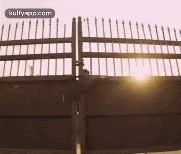 the sun is shining through the fence of a building .