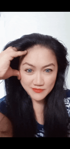 a woman with long black hair and blue eyes holds her hand to her head
