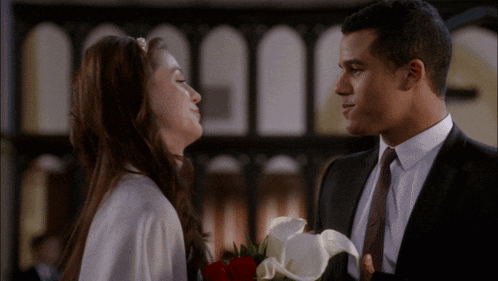 a man in a suit and tie is holding a bouquet of flowers and kissing a woman in a white dress