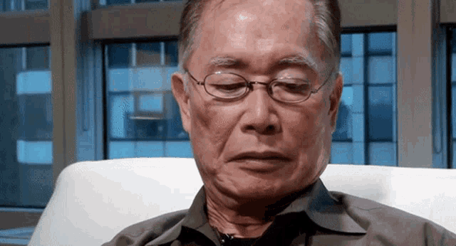 an older man wearing glasses sits in a chair