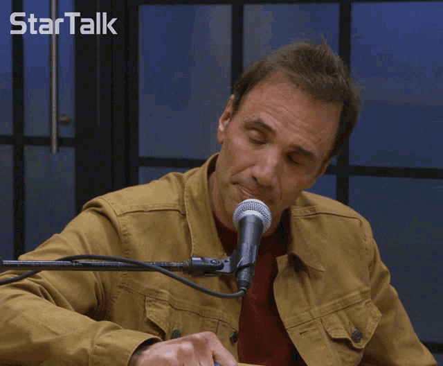 a man is smiling in front of a microphone with the word startalk behind him