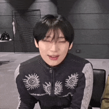 a young man wearing a black sweater with suns on it is making a funny face
