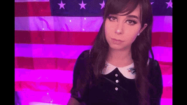 a girl is standing in front of an american flag and making a funny face .