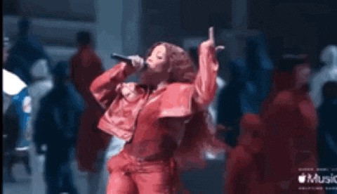 a woman in a red jacket is singing into a microphone while standing in front of a crowd .