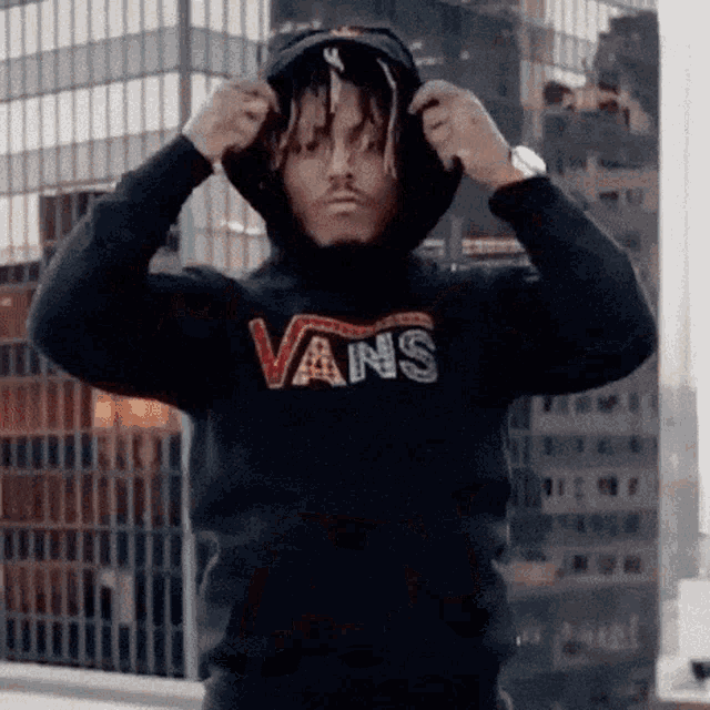 a man wearing a black vans hoodie is adjusting his hood .
