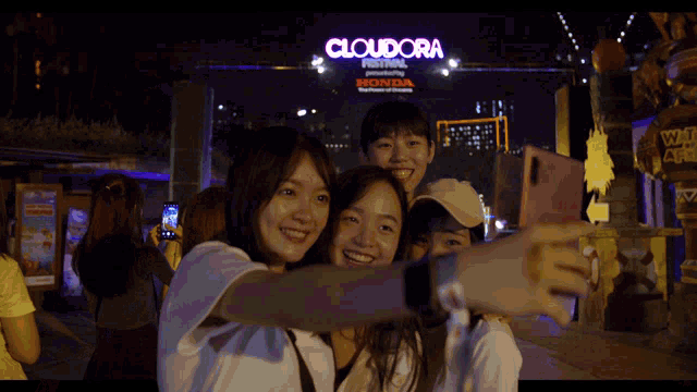 a group of people take a selfie in front of a cloudora festival sign