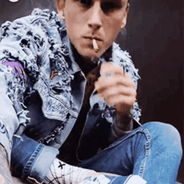 a man wearing a denim jacket and converse shoes is smoking a cigarette