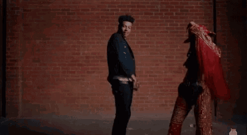a man and a woman are dancing together in front of a brick wall .