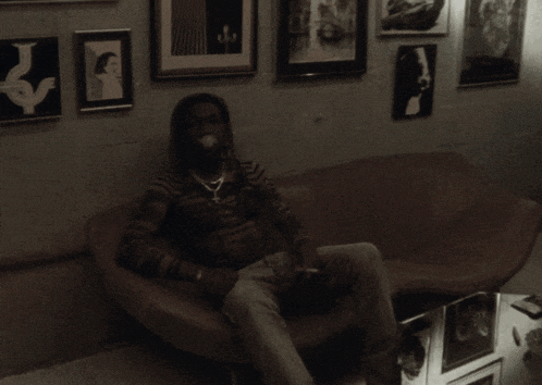 a man with dreadlocks sits on a couch in front of pictures on the wall