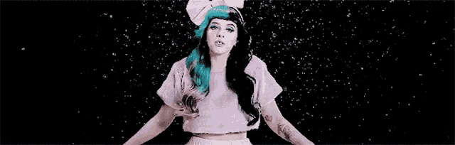 a woman with blue and black hair is wearing a pink crop top and a white bow on her head .
