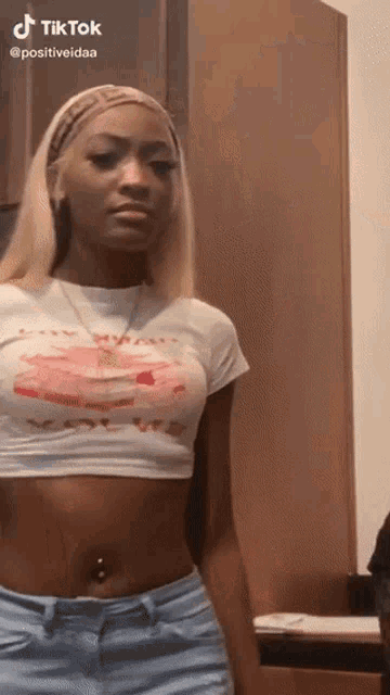 a woman in a white crop top and blue jeans is standing in a room .