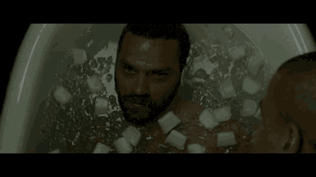 a man is laying in a bathtub with ice cubes on his body