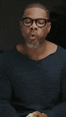 a man wearing glasses holds a green apple in his hands