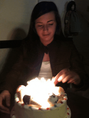 a woman blows out candles on a cake in the dark