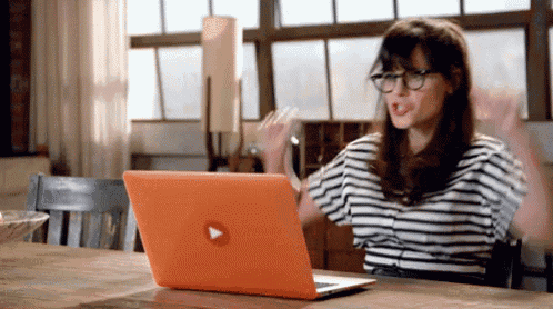 a woman is sitting at a table with an orange laptop with a play button on it