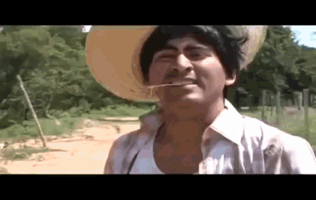a man wearing a straw hat and a white shirt is smoking a cigarette on a dirt road .