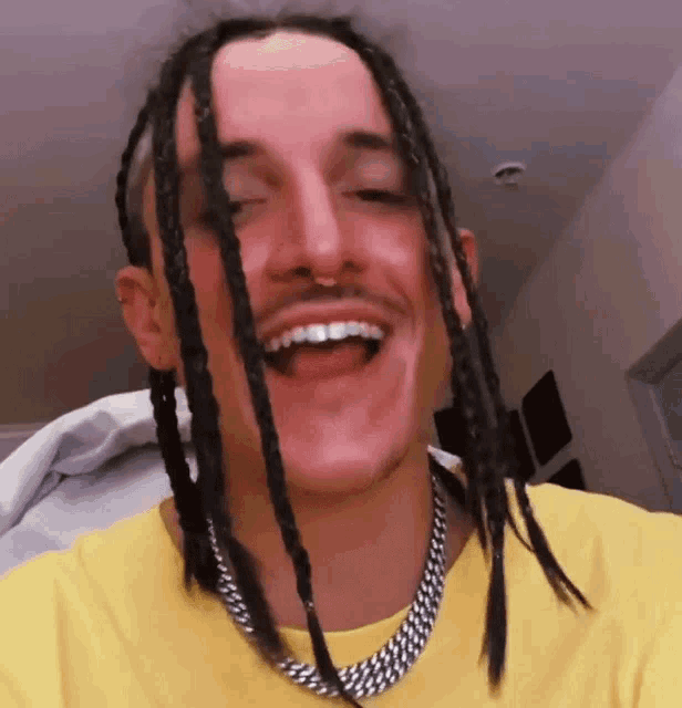 a man with dreadlocks and a chain around his neck is smiling
