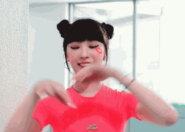 a woman in a red t-shirt is making a heart shape with her hands .