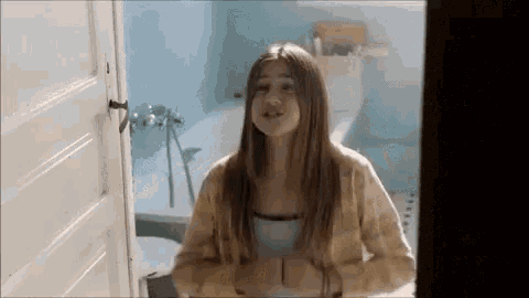 a girl is standing in a bathroom next to a bathtub and toilet .