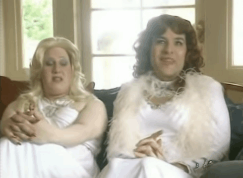 two women dressed in white are sitting on a couch smoking cigarettes