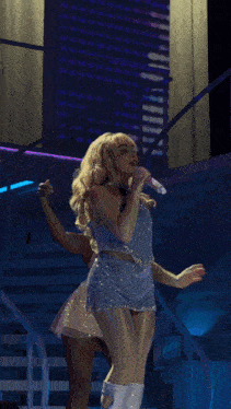 a blonde woman singing into a microphone on stage
