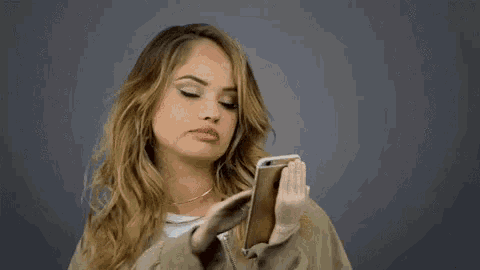 a woman is holding a cell phone in her hands and making a face .