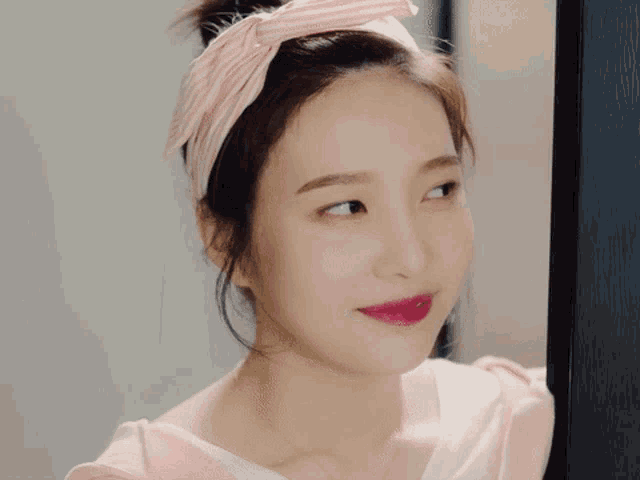 a woman wearing a pink striped headband looks at herself in the mirror
