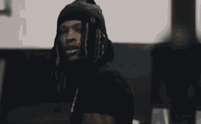 a man with dreadlocks and a necklace is wearing a black hat and a black shirt .