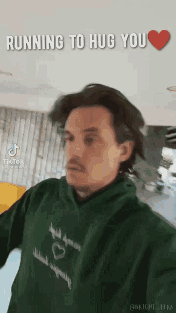 a man in a green hoodie is running to hug a woman .