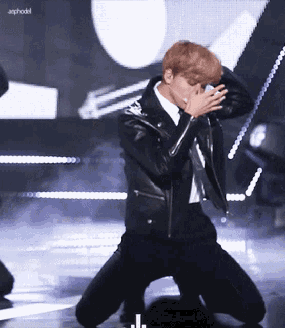 a man in a leather jacket is kneeling down and covering his mouth