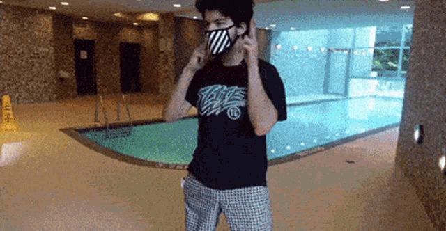 a man wearing a mask and a shirt that says ' the ' on it is standing in front of a pool