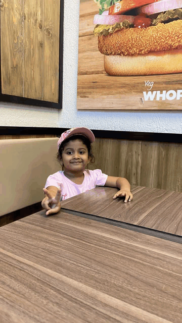 a little girl sitting at a table in front of a sign that says veg whof