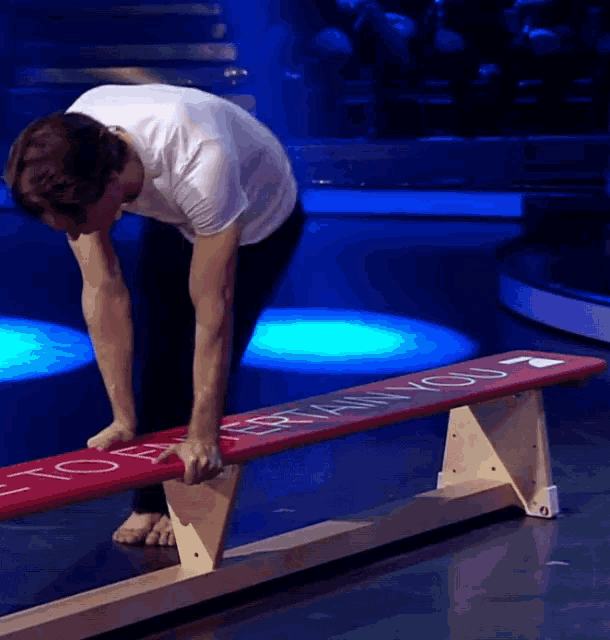 a man stands on a wooden balance beam with a red sign that says " i love you " on it