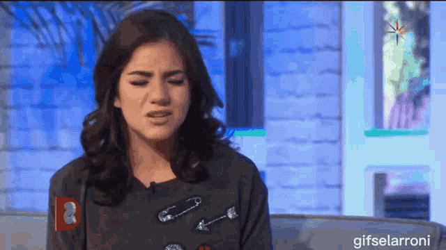 a woman is sitting on a couch with safety pins on her sweater