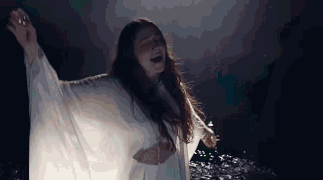 a woman in a white dress is laughing with her arms outstretched .