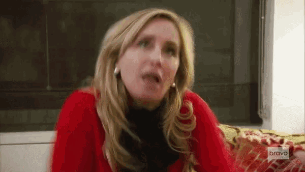a woman is sitting on a couch wearing a red sweater and making a funny face .