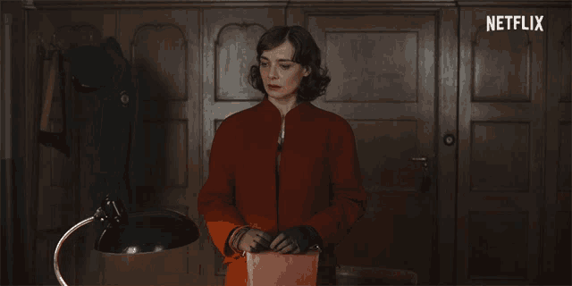 a woman in a red coat and black gloves is standing in front of a netflix logo