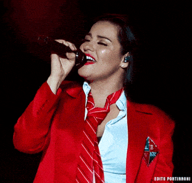 a woman in a red jacket and tie is singing into a microphone with the words edits portirroni below her