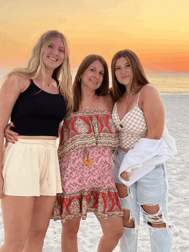 three women posing for a picture on the beach with one wearing a floral dress