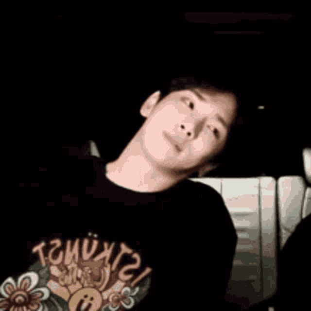 a man wearing a black t-shirt with a flower on it is sitting in a car .