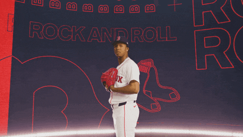 a man in a red sox uniform stands in front of a wall that says rock and roll