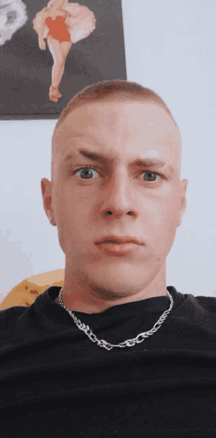 a man wearing a black shirt and a silver chain around his neck looks at the camera