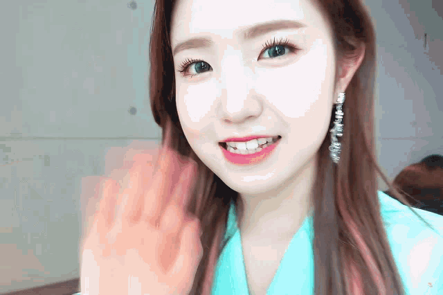 a young woman wearing a blue shirt and earrings is smiling and waving .