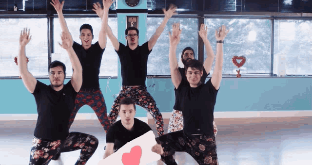 a group of men are posing with their arms in the air and one of them is holding a sign with a heart on it