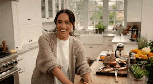 a woman in a sweater is smiling while standing in a kitchen